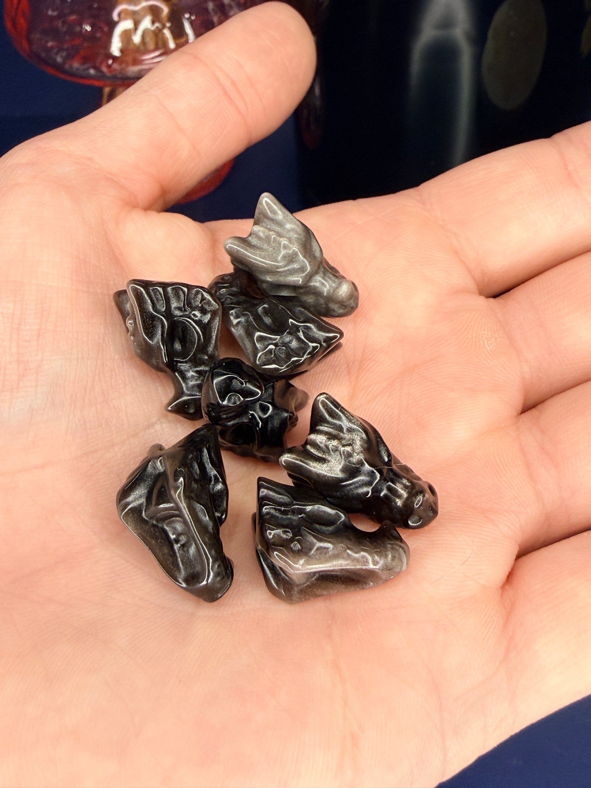 Hand holding several black obsidian mini dragon head carvings in front of a pink vase and black jar