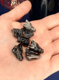 Hand holding several black obsidian mini dragon head carvings in front of a pink vase and black jar