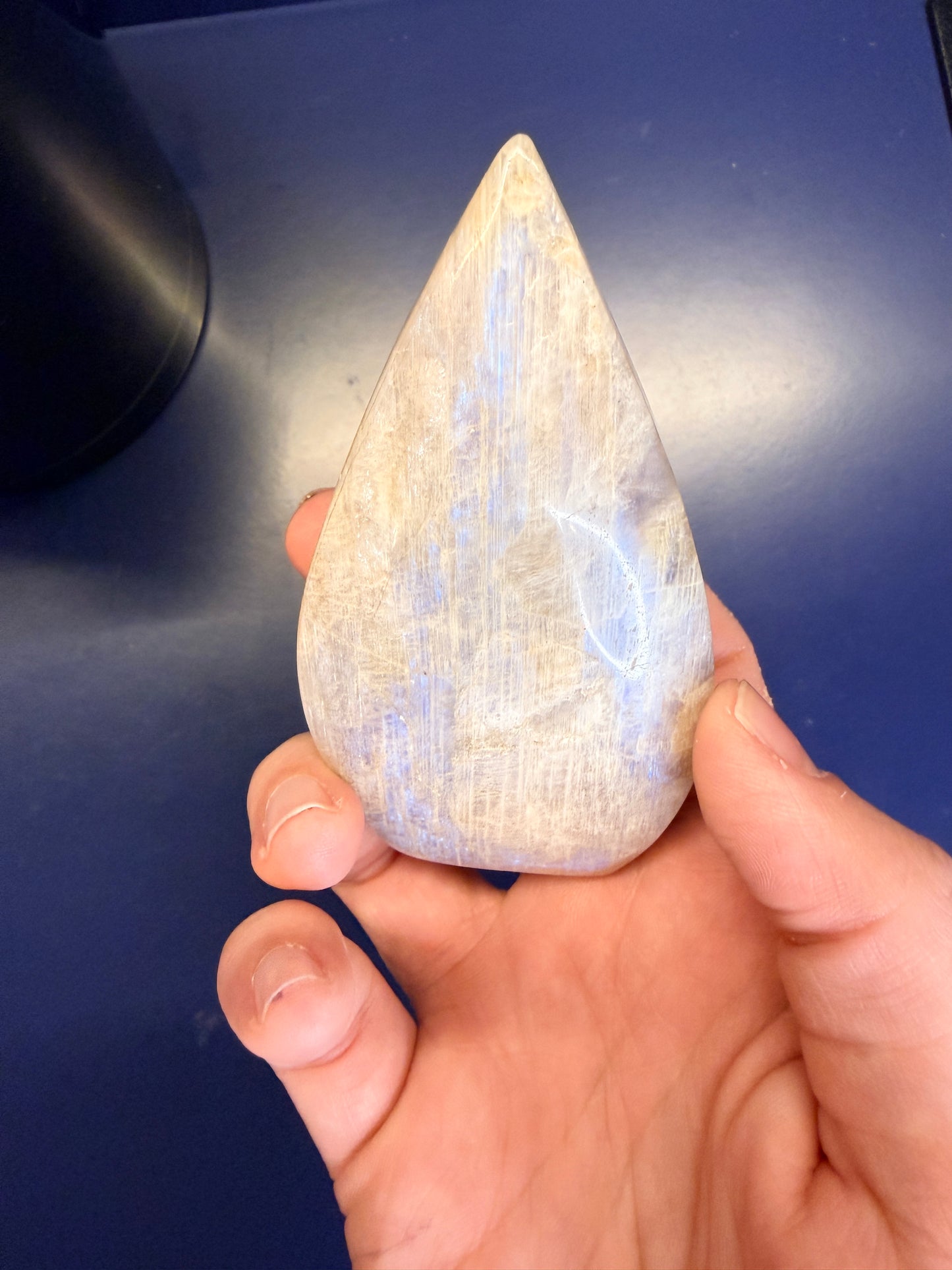 Hand holding a pointed moonstone crystal with a blue flash against a blue background