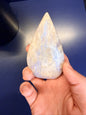 Hand holding a pointed moonstone crystal with a blue flash against a blue background
