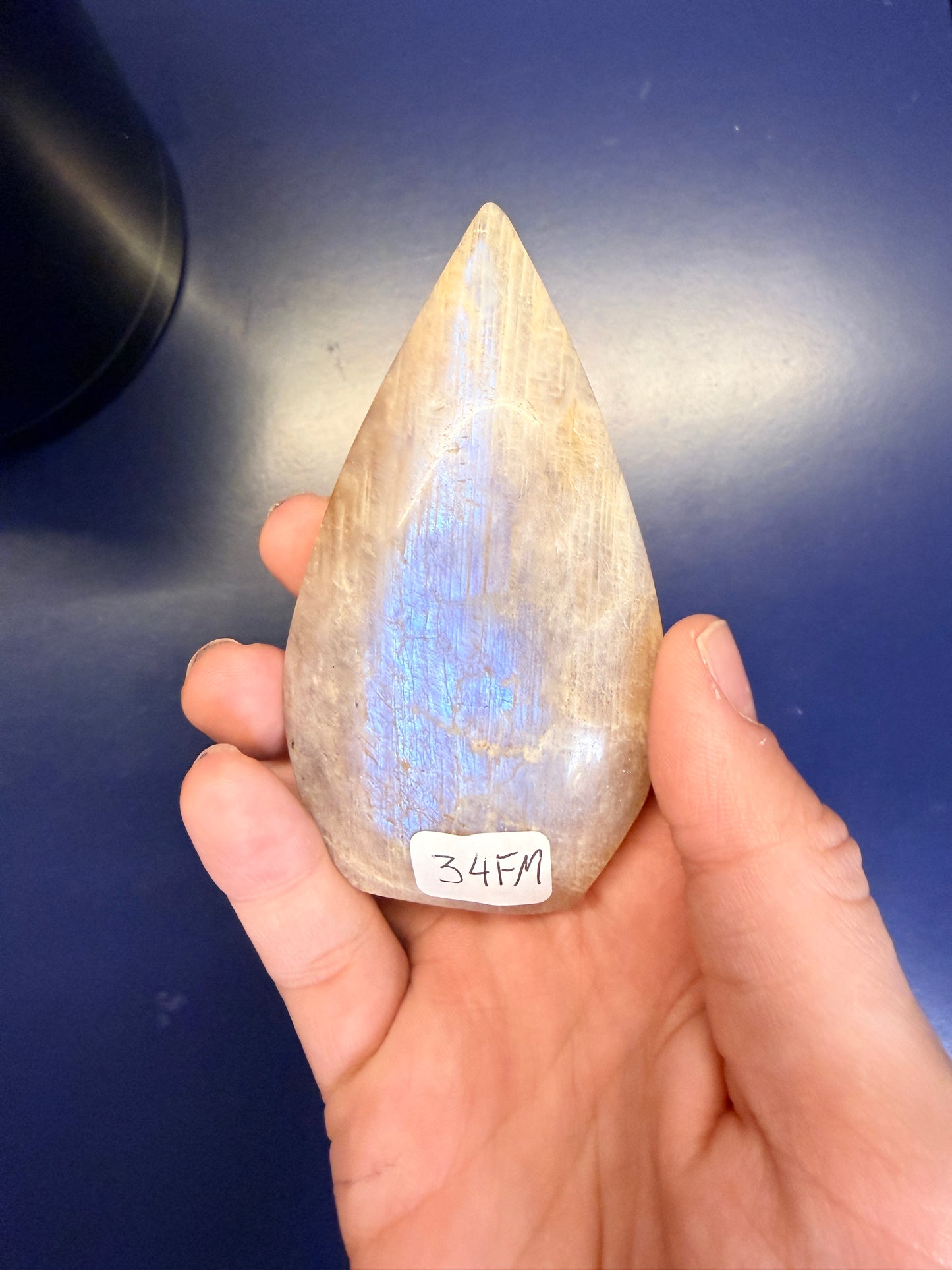 Hand holding a pointed moonstone crystal with a blue flash against a blue background