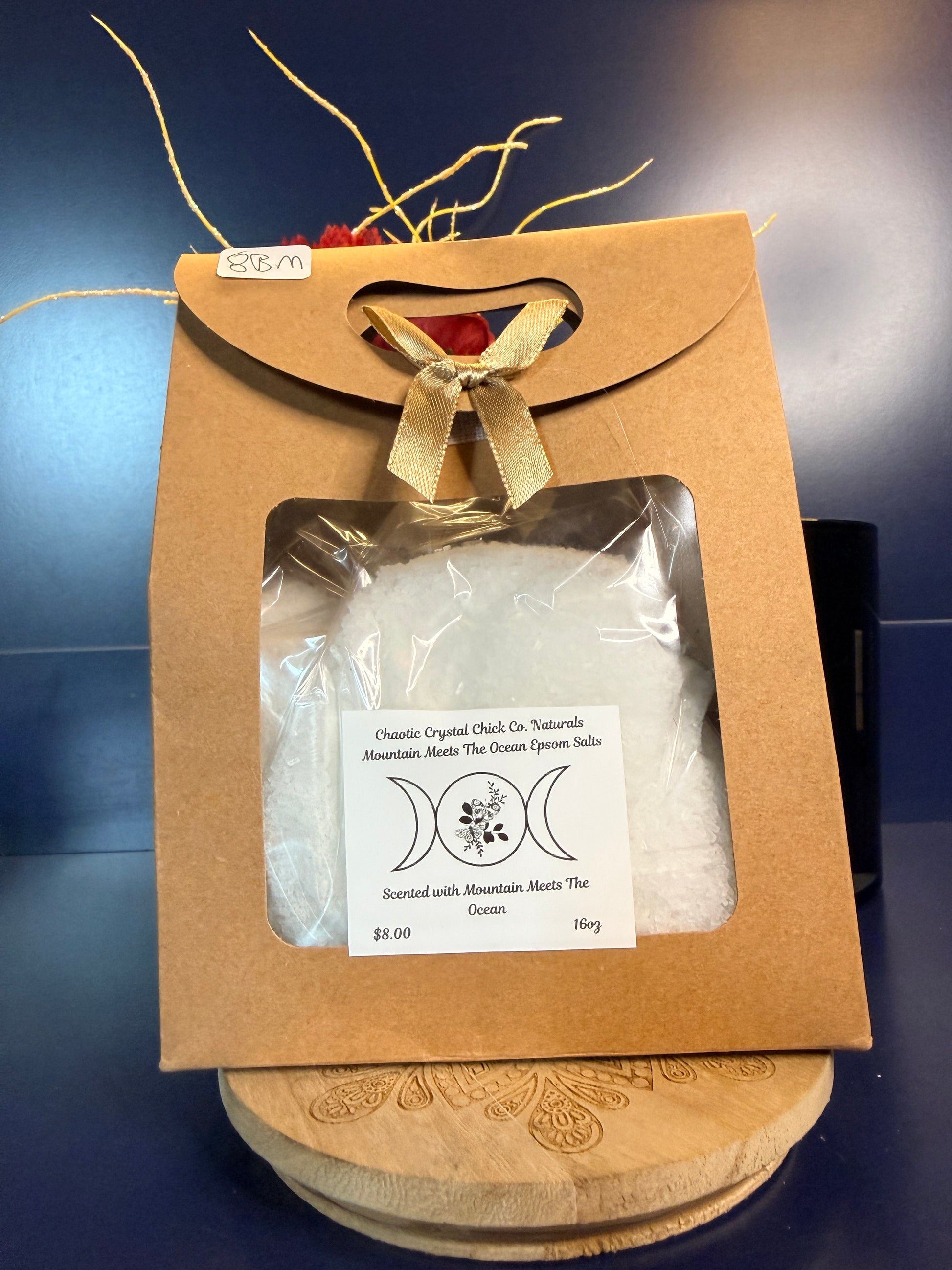 White epsom salt in a brown paper container with a bow, on a wooden coaster