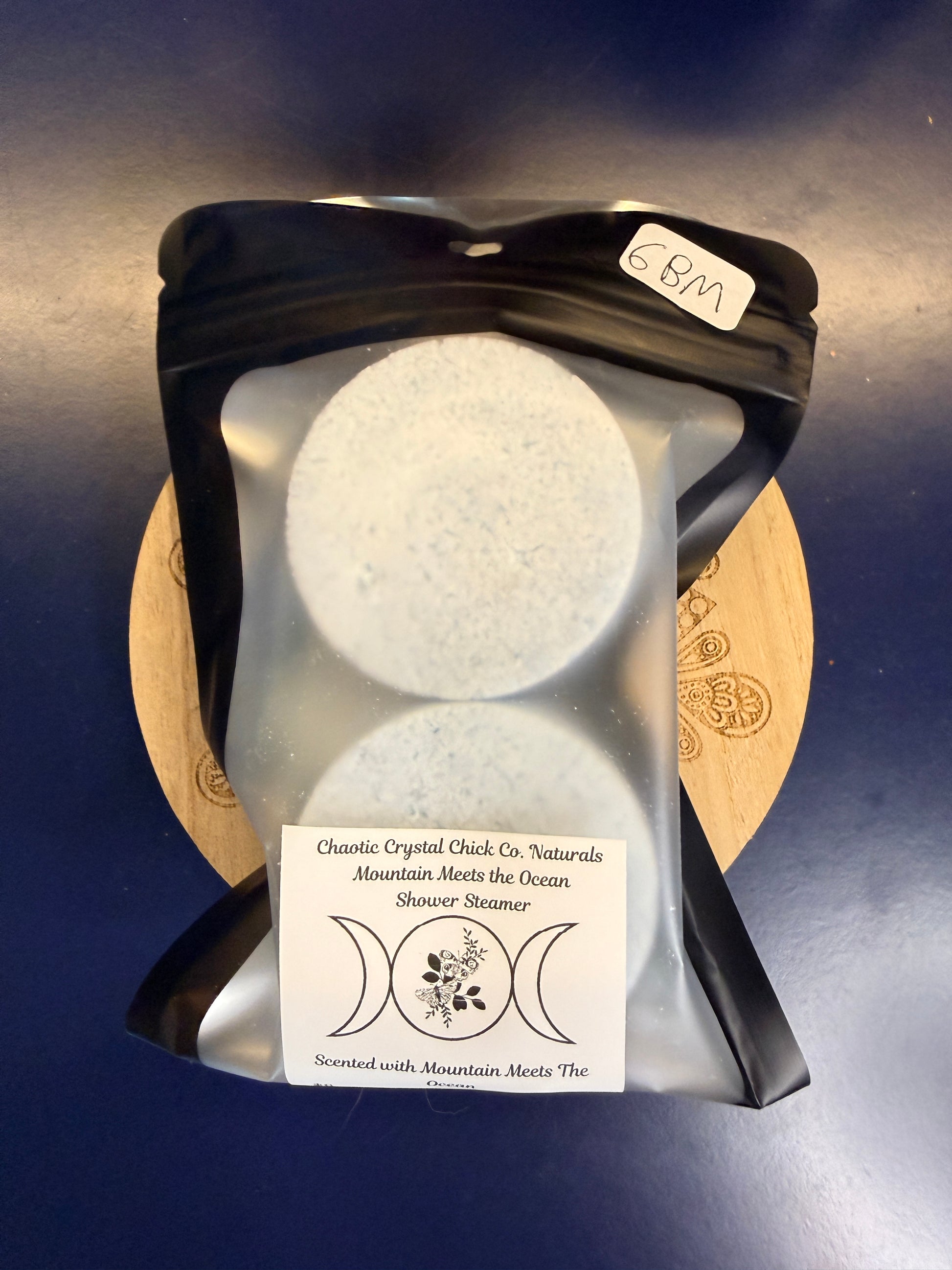 Packaged blue shower steamers on a decorative wooden coaster on a blue background
