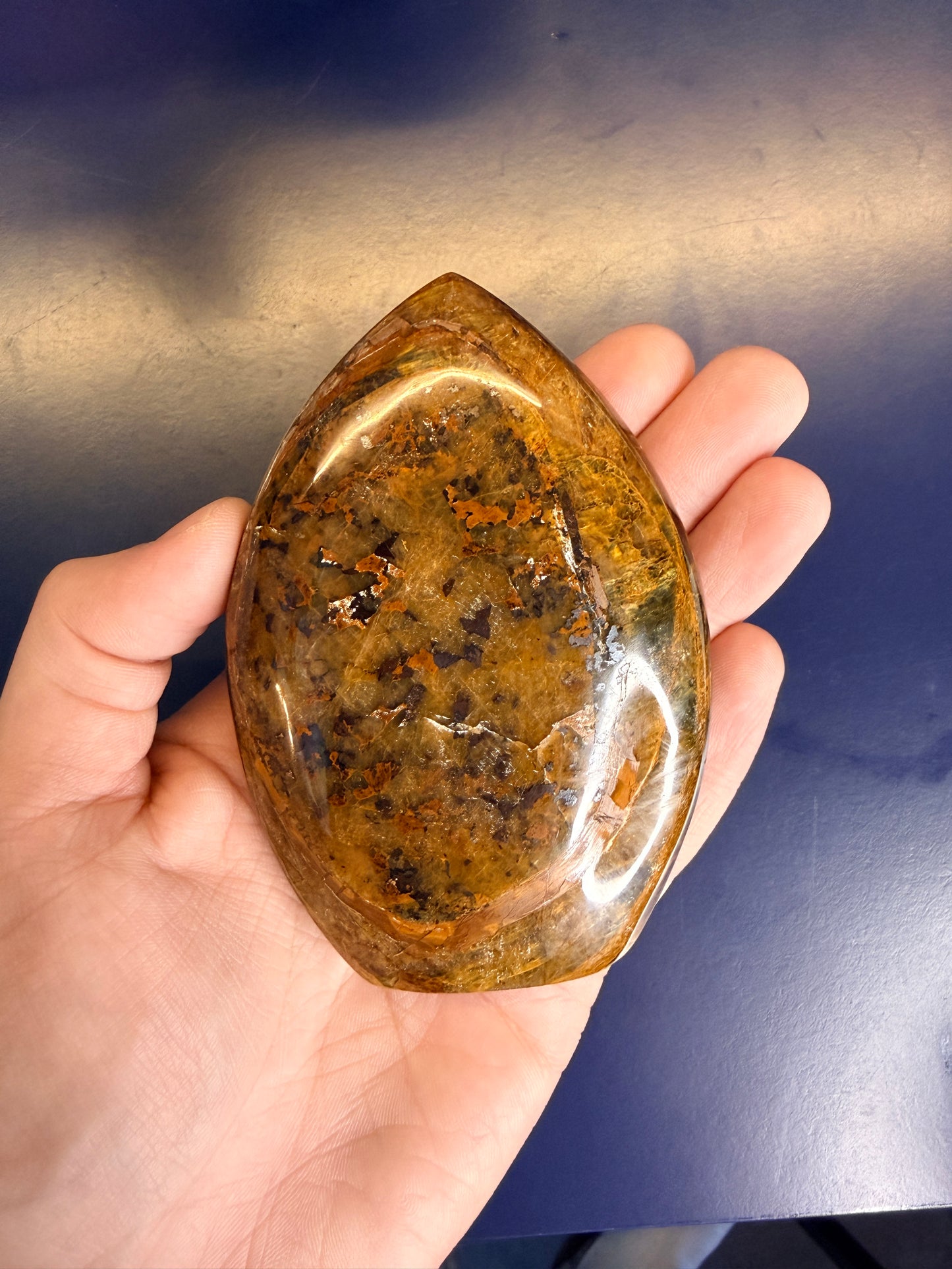 Hand holding gold nellite freeform against a blue background