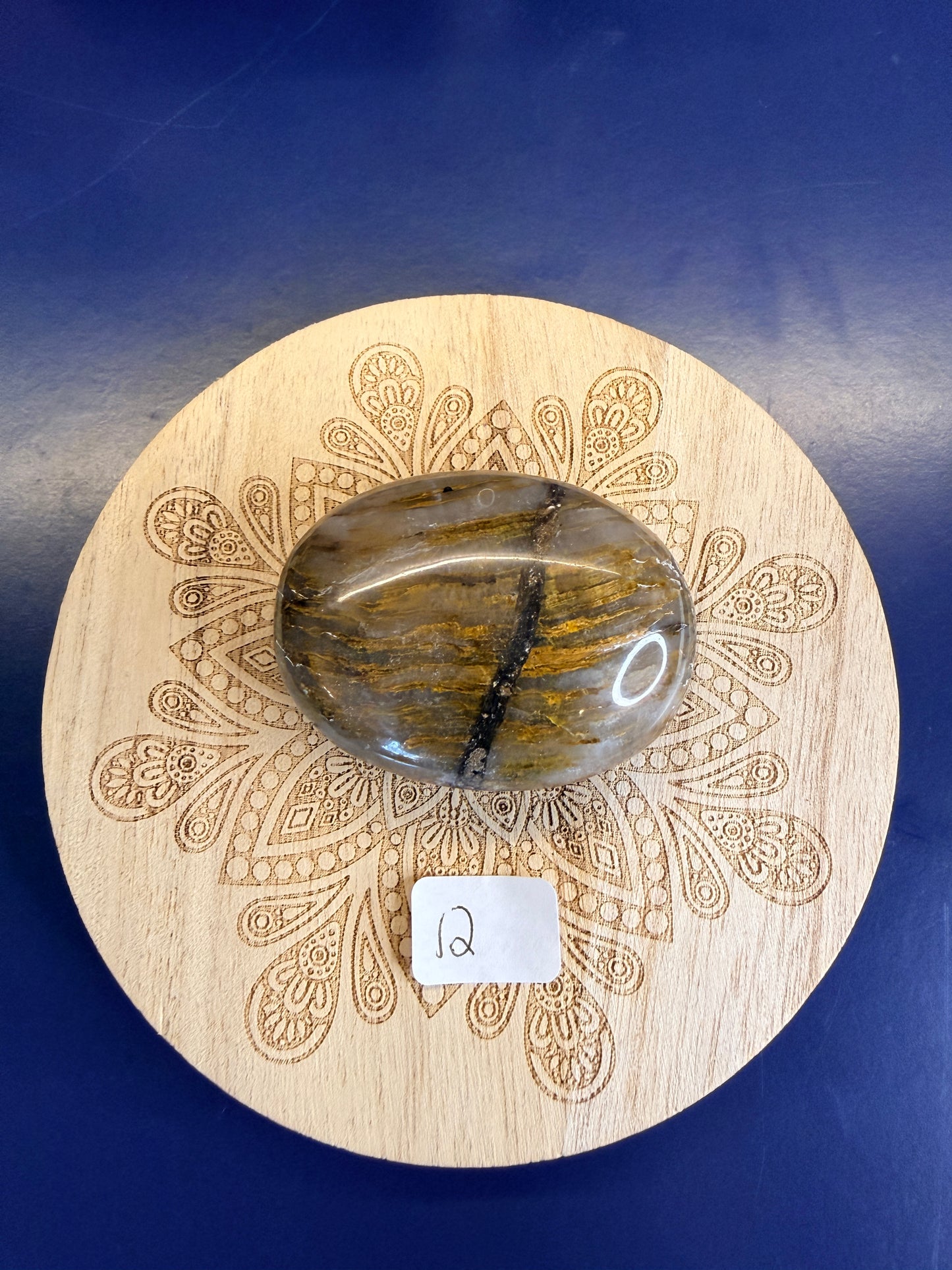 Decorative wooden coaster with a gold and clear nellite palmstone on a blue background