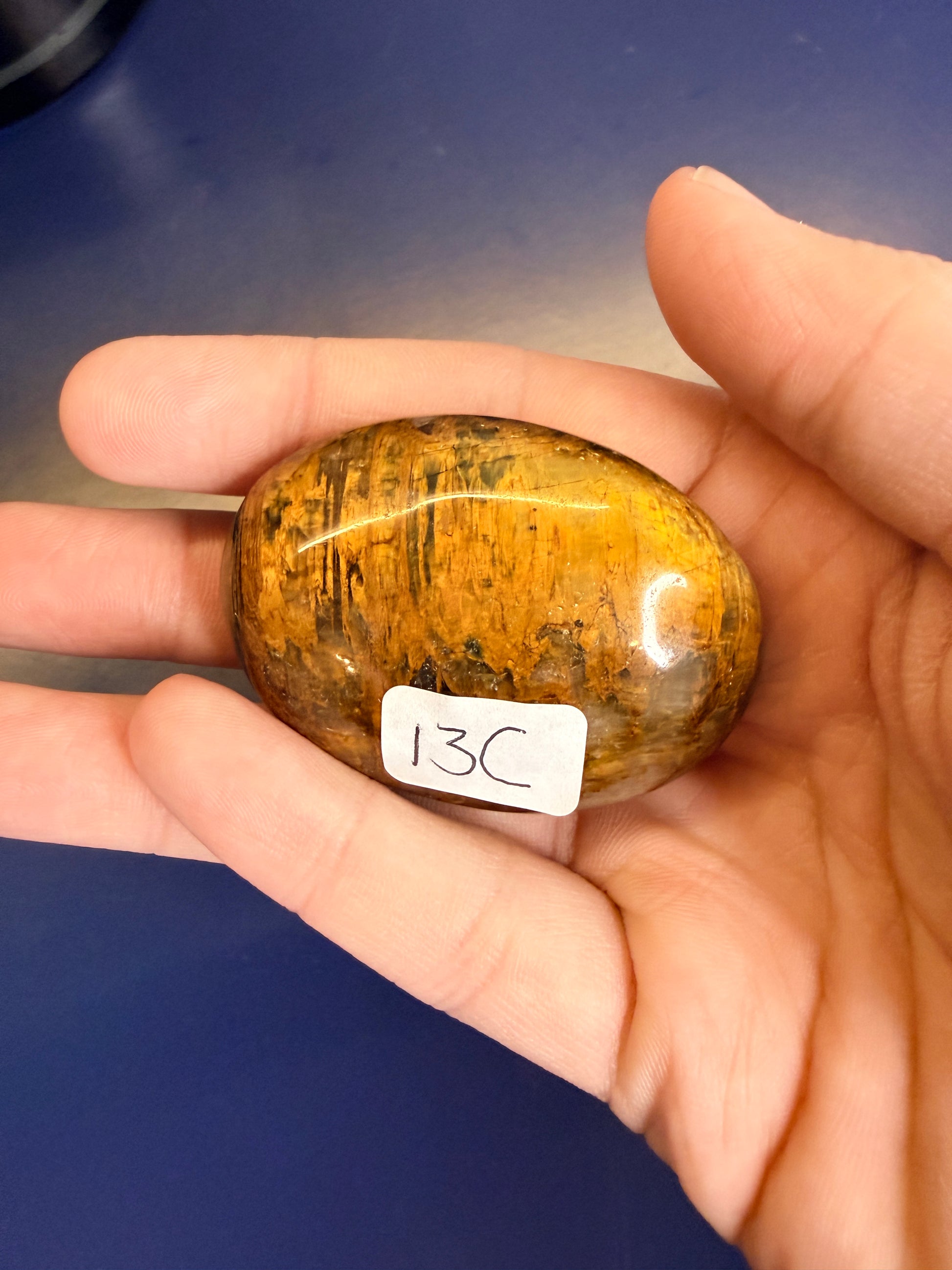 Hand holding a gold nellite palmstone on a blue background