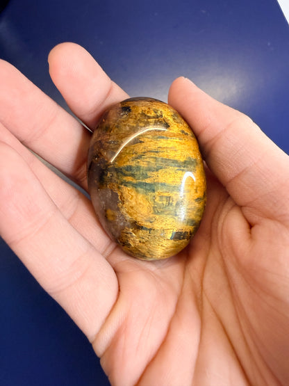 Hand holding a gold nellite palmstone on a blue background