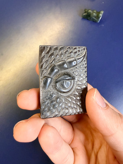 Hand holding a black and silver obsidian dragon eye slab against a blue background