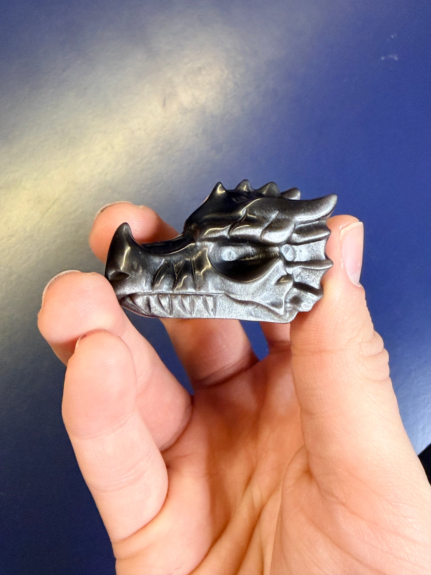 Hand holding an obsidian dragon-shaped crystal against a blue background