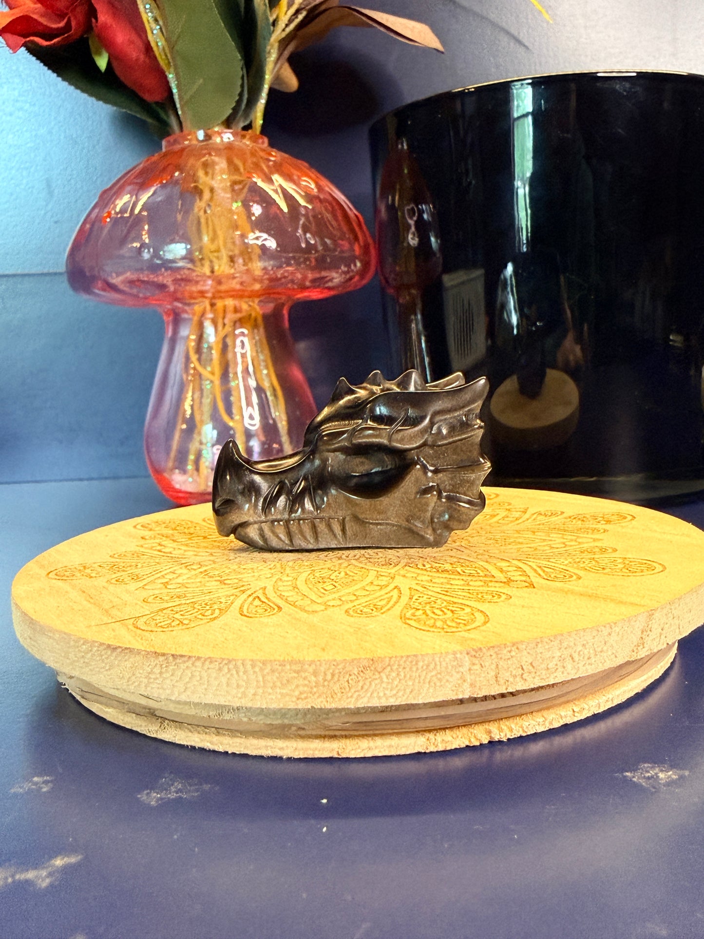 An obsidian dragon-shaped crystal sitting on a decorative wooden coaster against a blue background