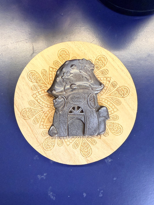A Silver and black obsidian mushroom house sitting on a decorative wooden coaster on a blue background