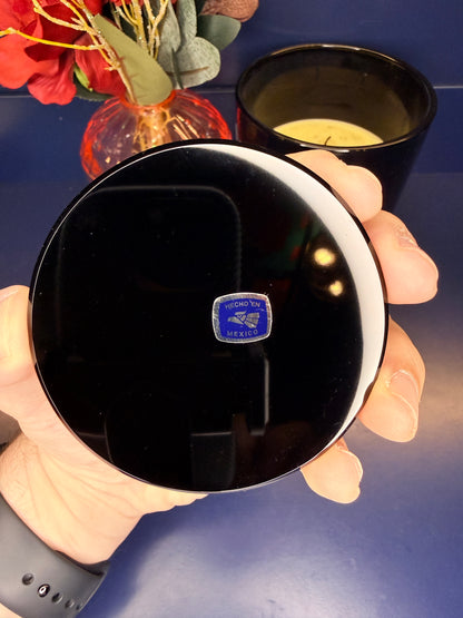 Hand holding a round black obsidian scrying mirror in front of a red flower and black candle jar