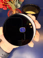 Hand holding a round black obsidian scrying mirror in front of a red flower and black candle jar