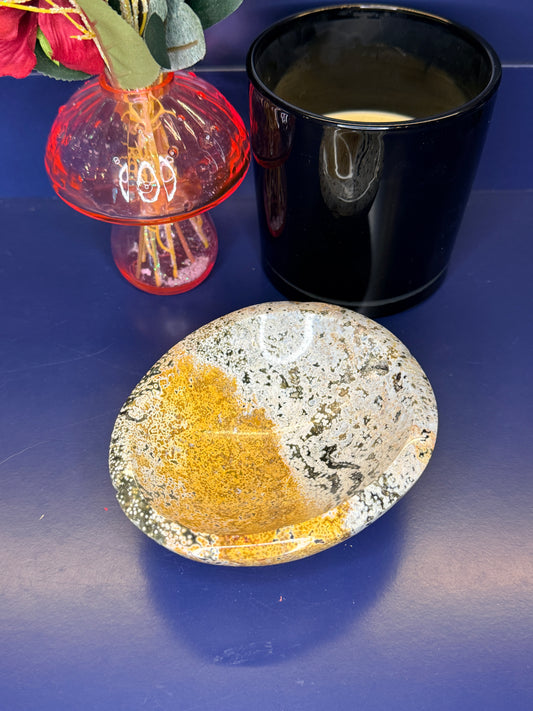 White, green, and yellow ocean jasper bowl in front of a pink mushroom vase and black jar on a blue background