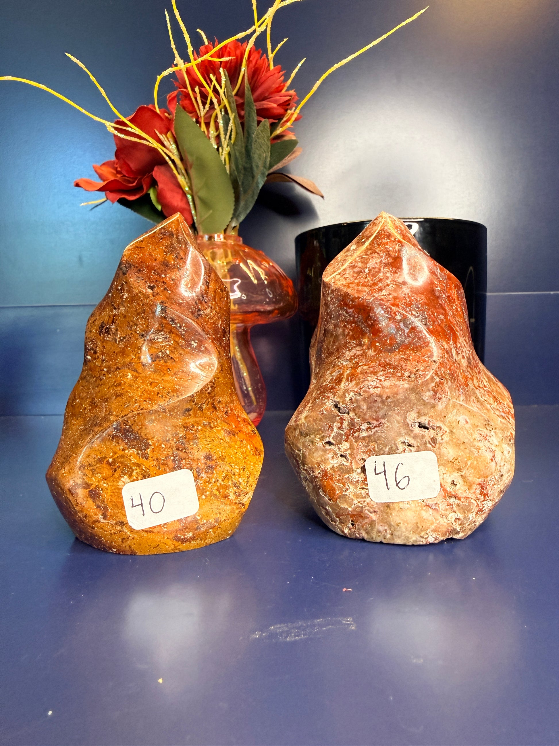 Two orange and red ocean jasper flames in front of a red flower and black jar on a blue background