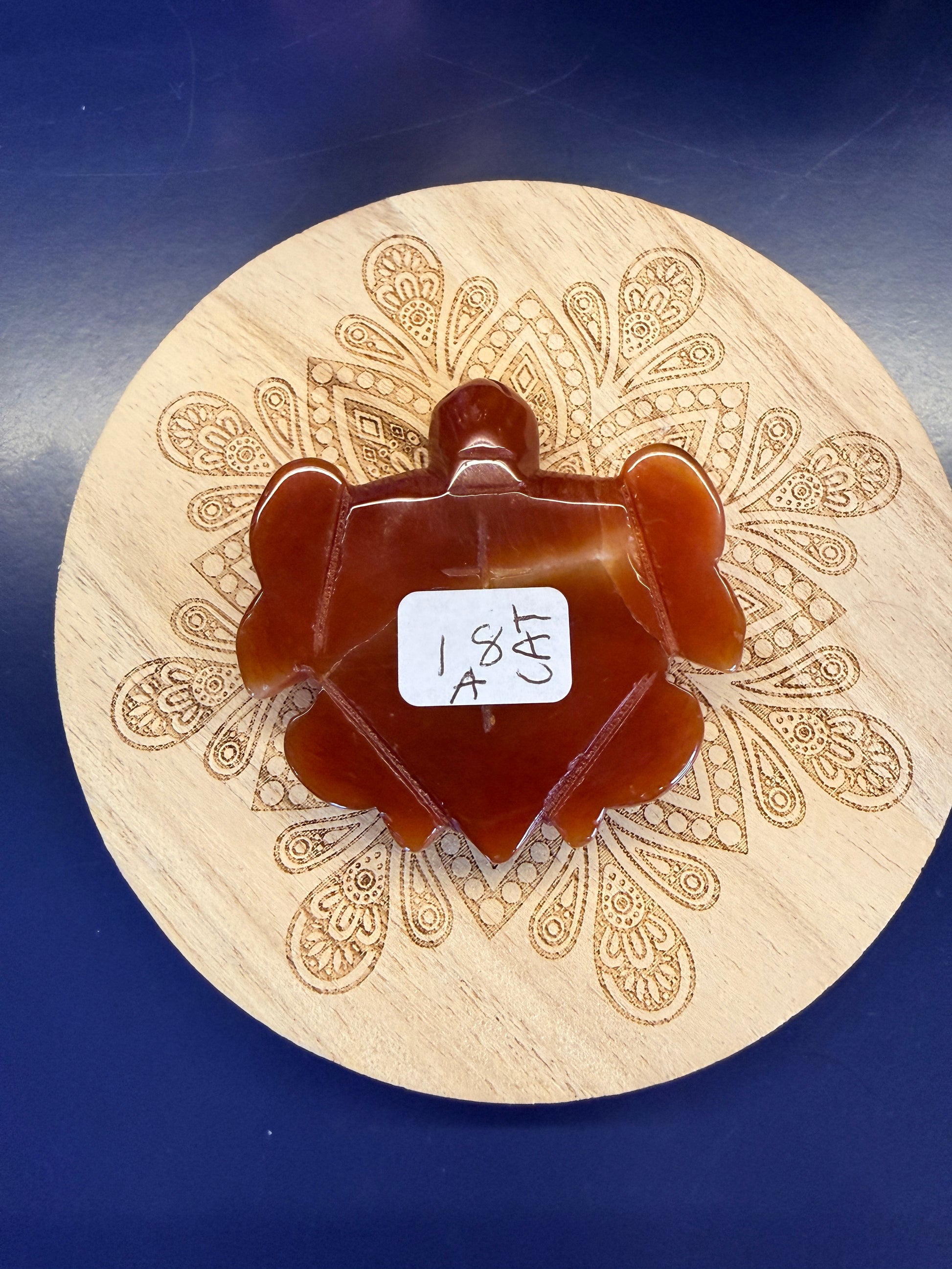 Red carnelian turtle sitting on a decorative wooden coaster on a blue background