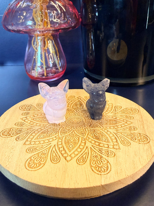 Two eevee crystal shapes sitting on a decorative wooden coaster in front of a glass mushroom and black jar