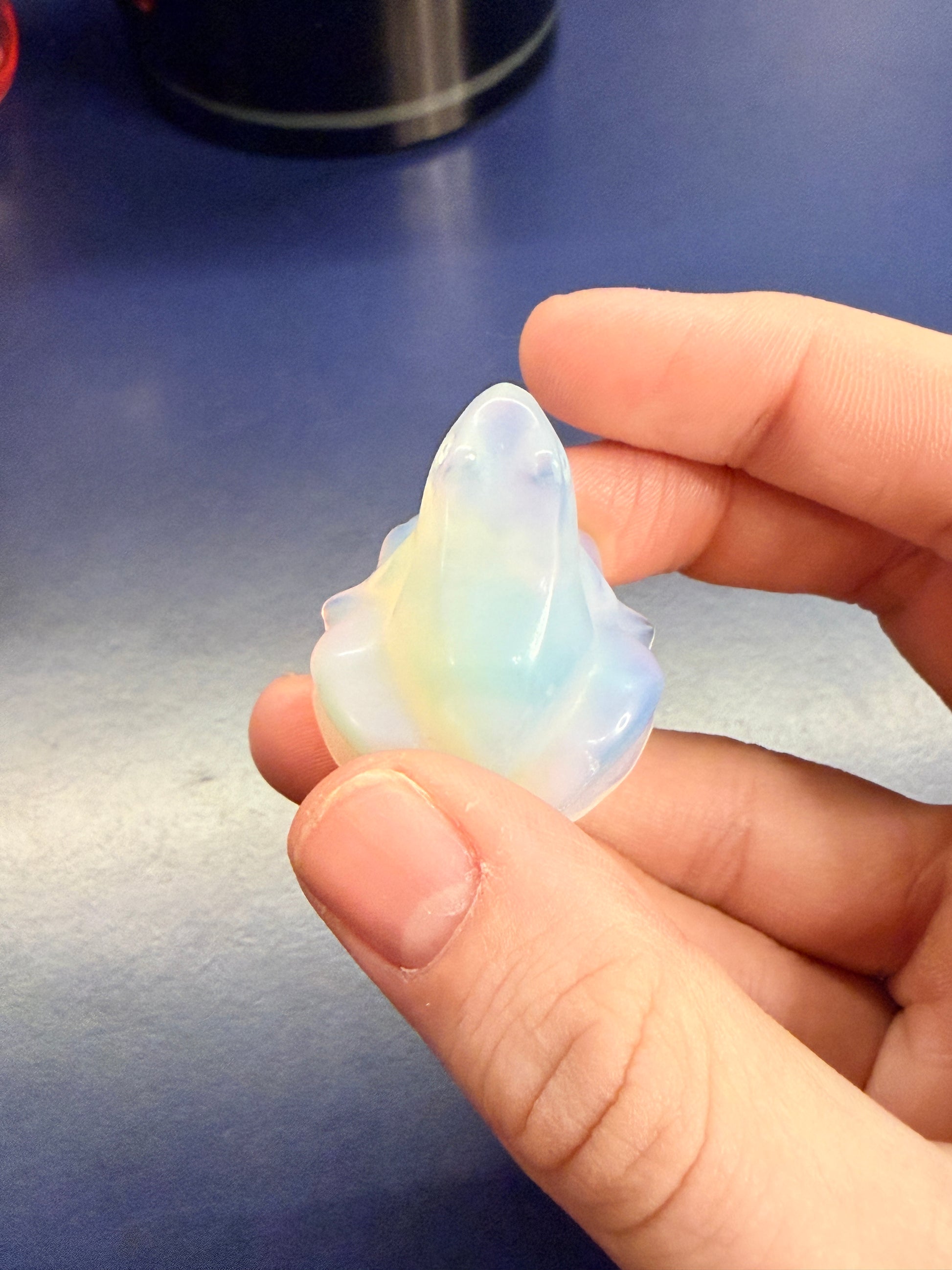 Hand holding an opalite frog crystal against a blue background