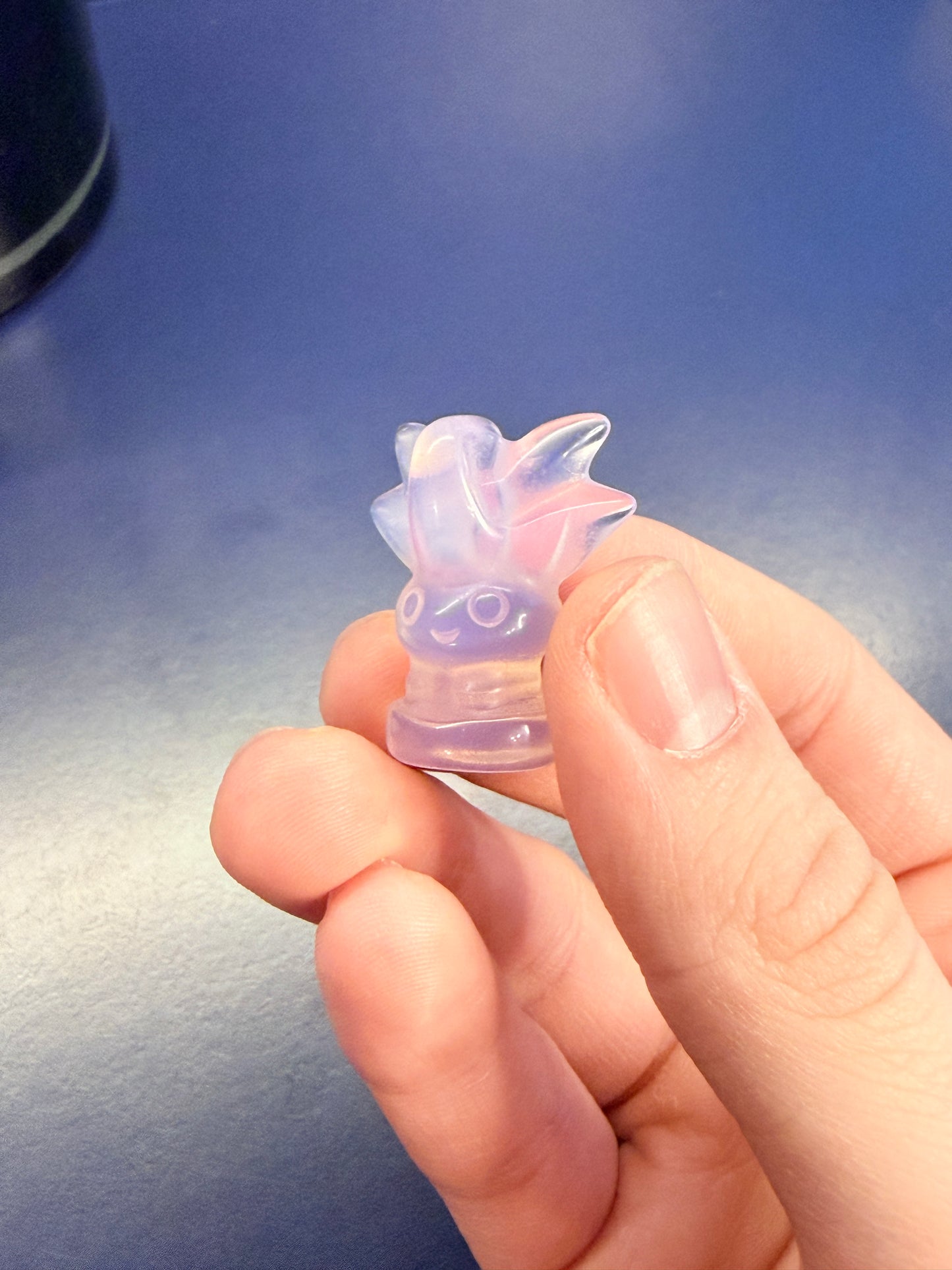 Hand holding translucent opalite oddish on blue background