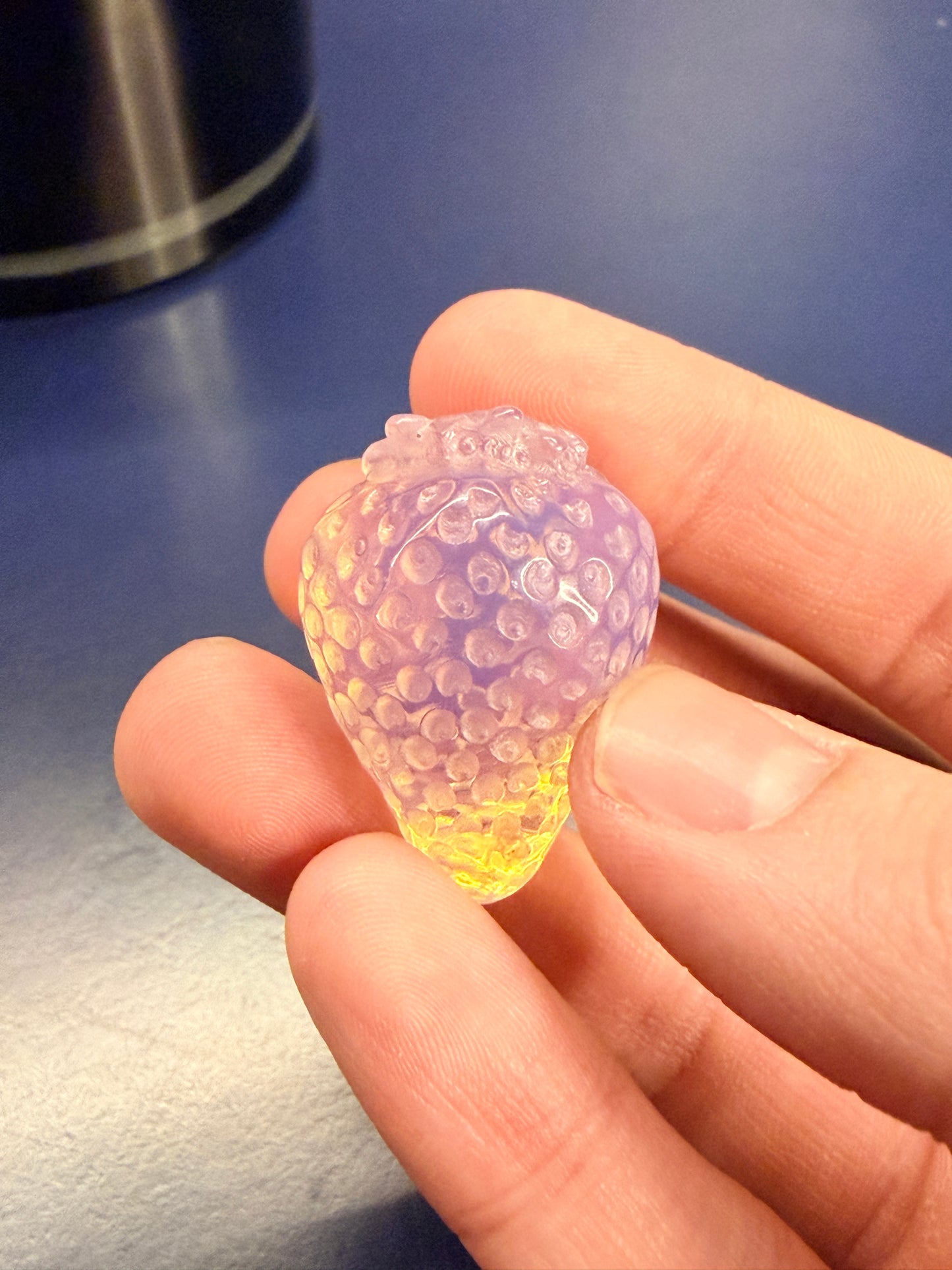Hand holding an opalite strawberry crystal against a blue background