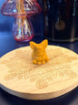 An orange calcite flareon crystal sitting on a decorative wooden coaster in front of a glass mushroom and black jar