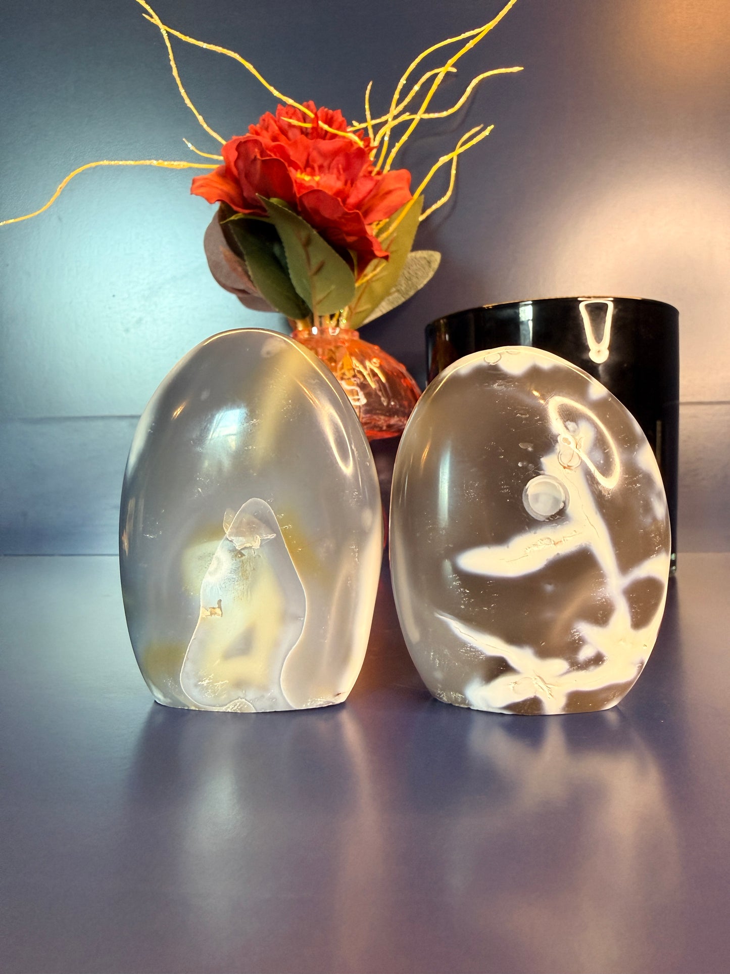 Two white and grey orca agate freeforms in front of a flower and black jar