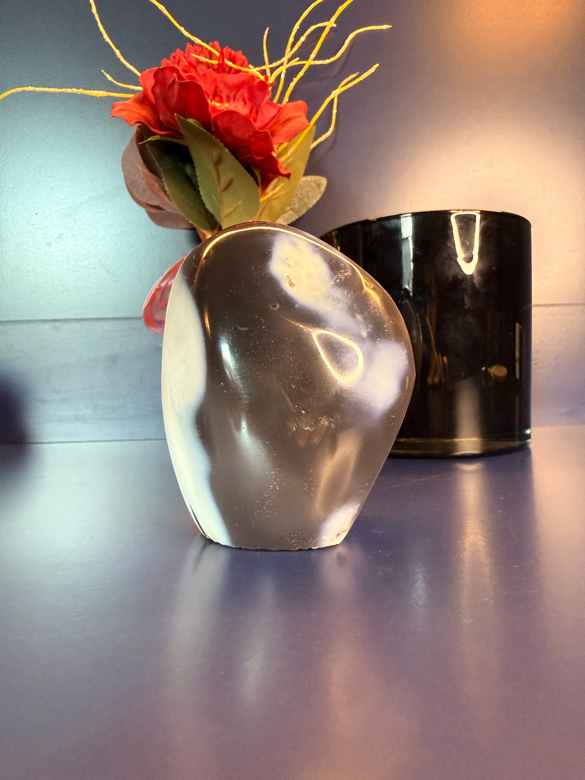 A white and grey orca agate freeform in front of a flower and black jar