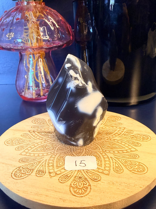 A white and black crystal flame sitting on a decorative wooden coaster in front of a glass mushroom and black jar