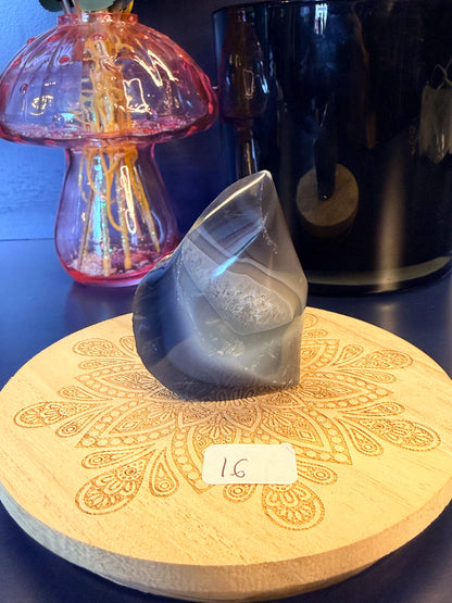 A white and black crystal flame sitting on a decorative wooden coaster in front of a glass mushroom and black jar