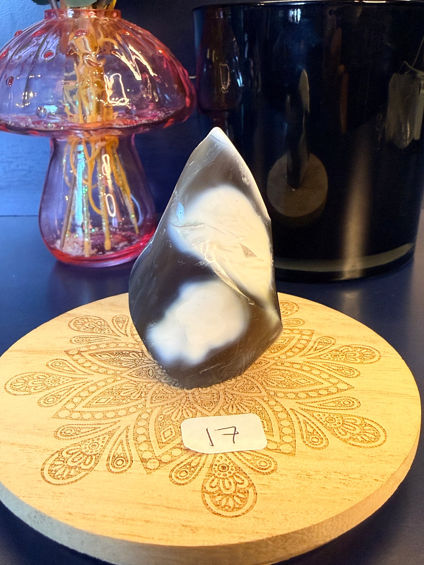 A white and black crystal flame sitting on a decorative wooden coaster in front of a glass mushroom and black jar