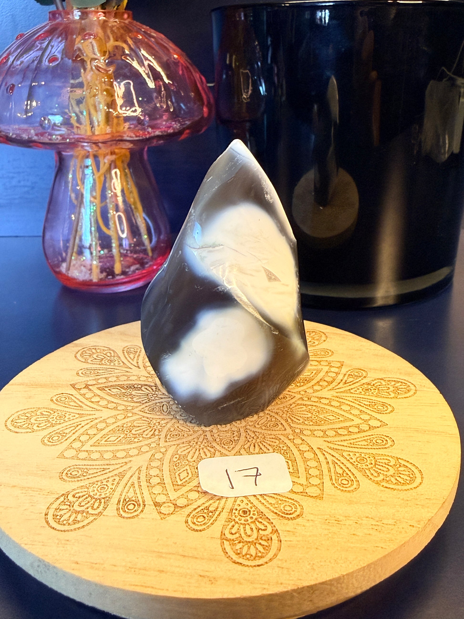 A white and black crystal flame sitting on a decorative wooden coaster in front of a glass mushroom and black jar