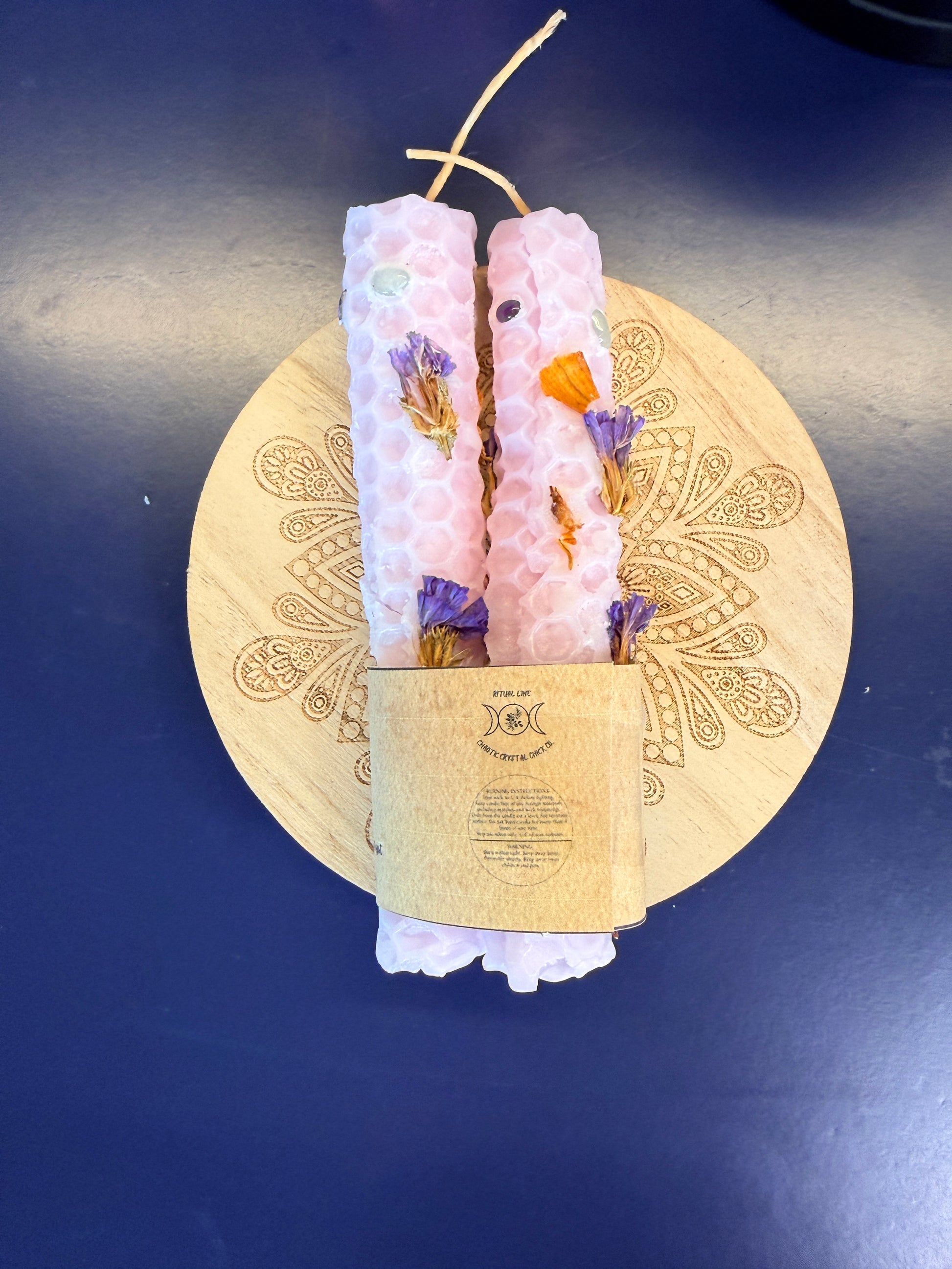 Two pink rolled candles sitting on a decorative wooden coaster on a blue background