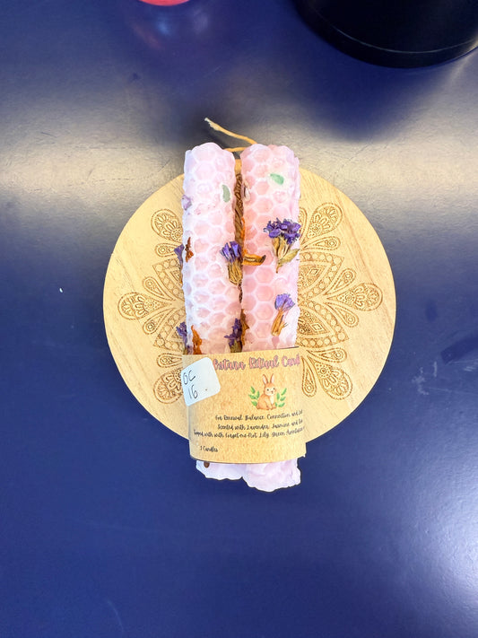 Two pink rolled candles sitting on a decorative wooden coaster on a blue background