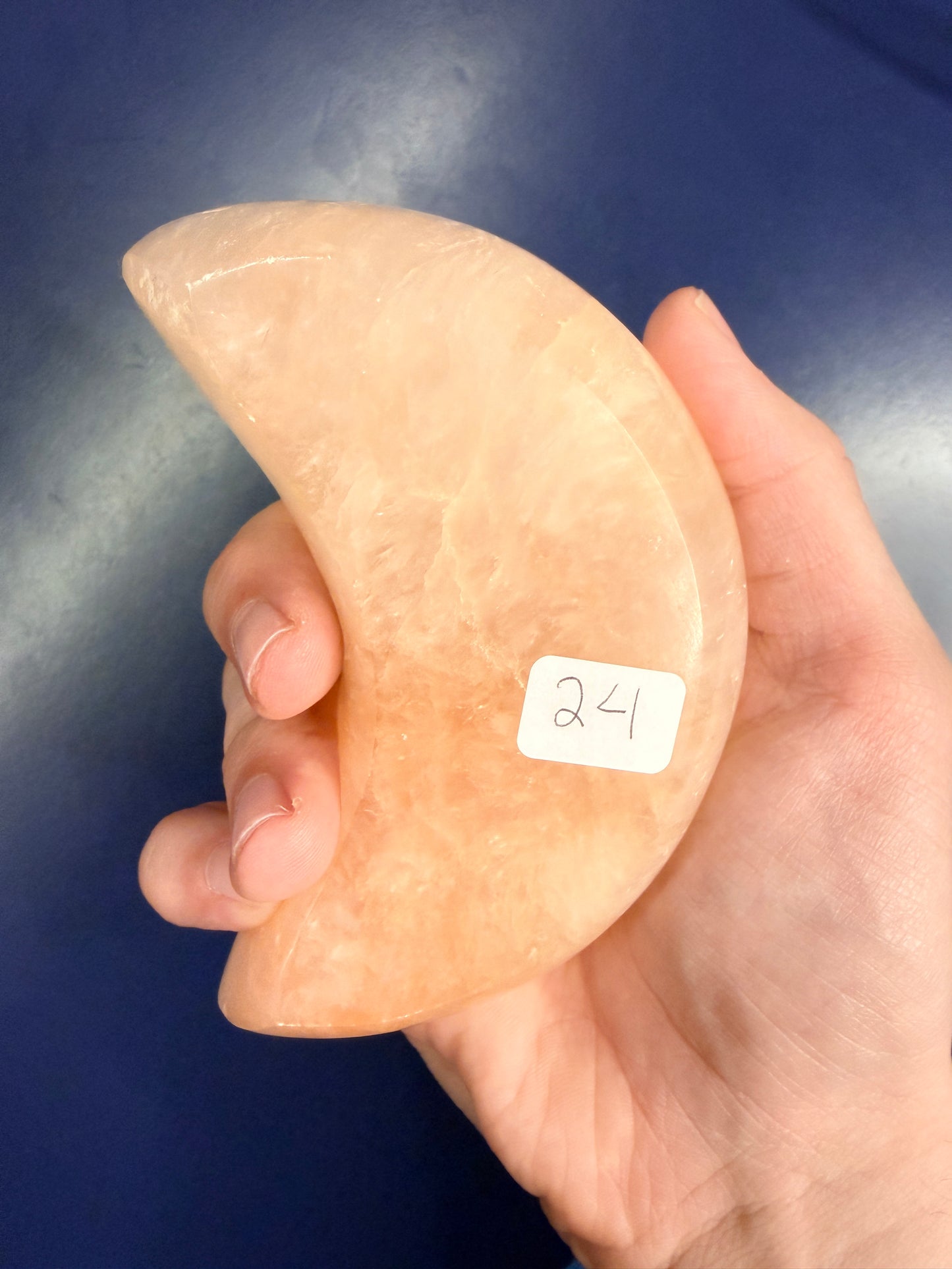 Hand holding a large peach selenite moon bowl with a "24" label on a blue background