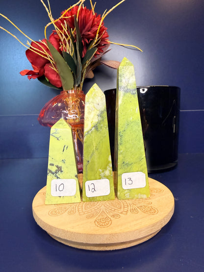 Three lime green opal towers on a wooden coaster in front of a red flower in a vase and black jar