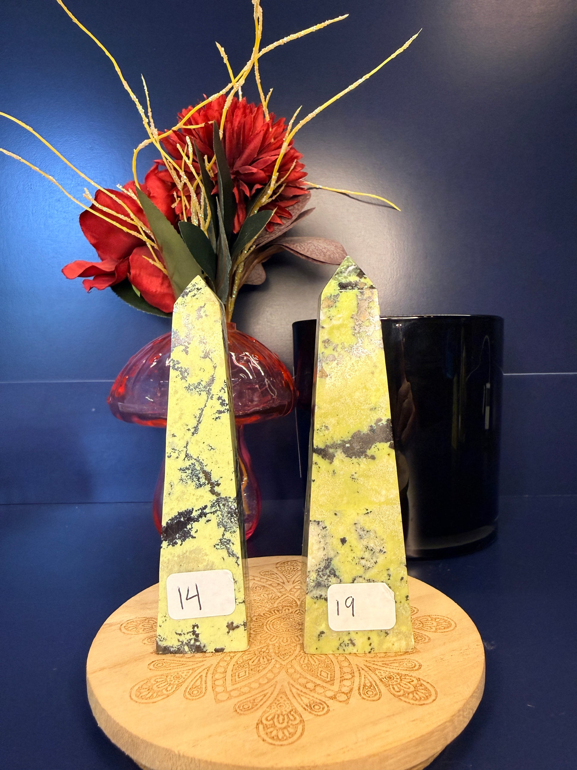 Two lime green opal towers on a wooden coaster in front of a red flower in a vase and black jar