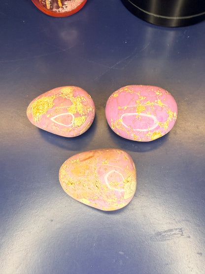 Three pink and tan phosphosiderite palmstones on a blue background