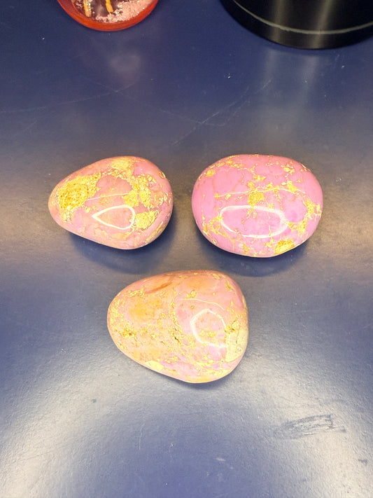 Three pink and tan phosphosiderite palmstones on a blue background