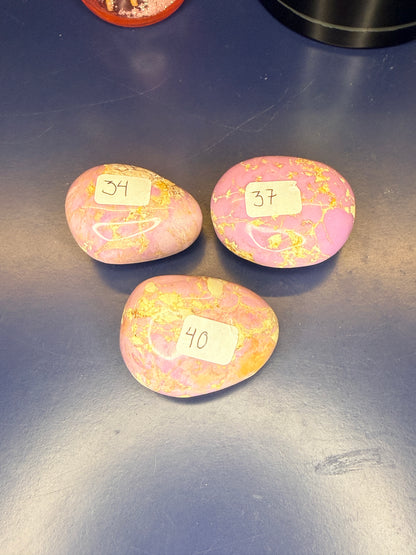 Three pink and tan phosphosiderite palmstones on a blue background