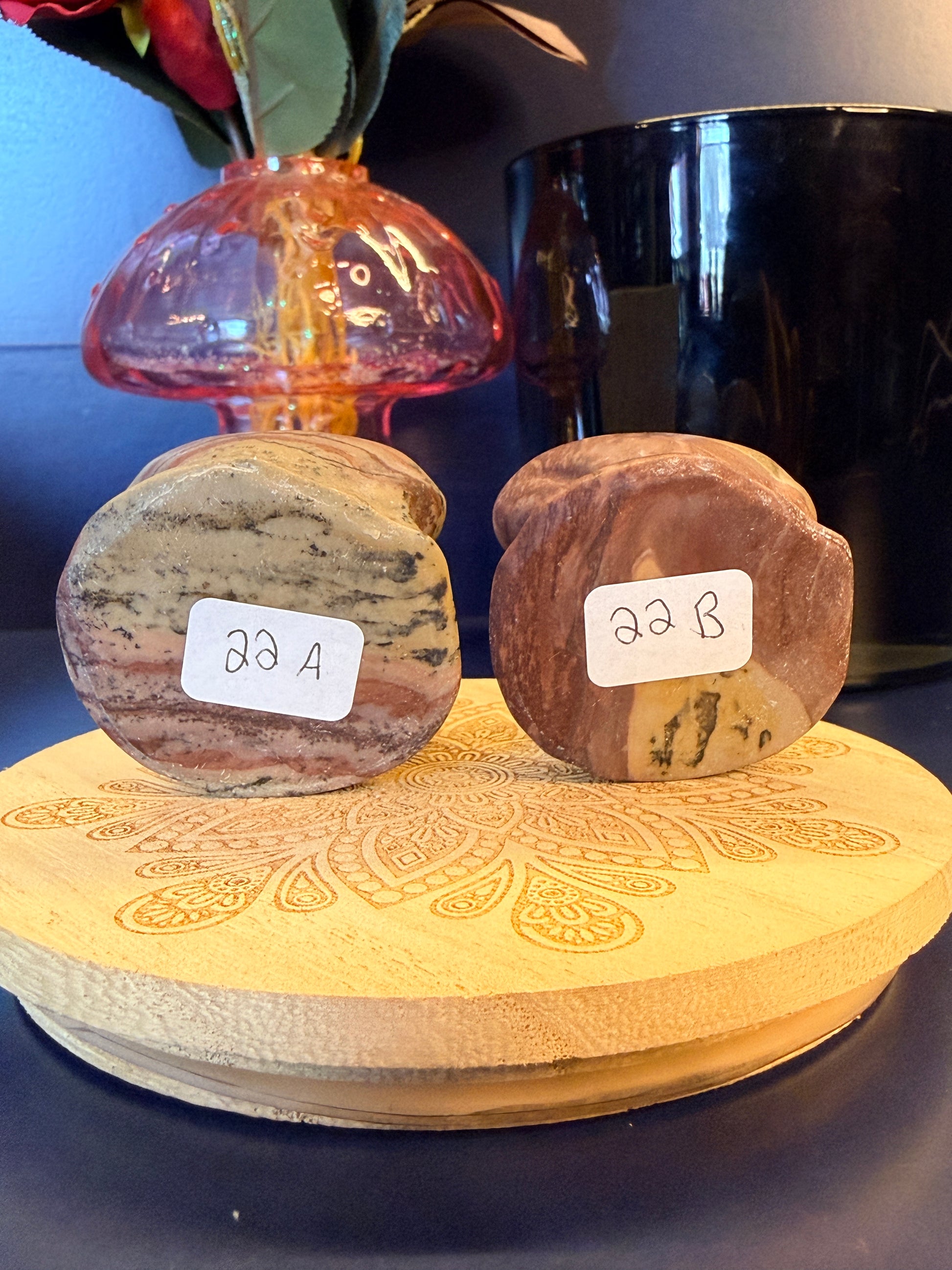 Two picture jasper frogs showing codes sitting on a decorative wooden coaster in front of a glass mushroom and black jar