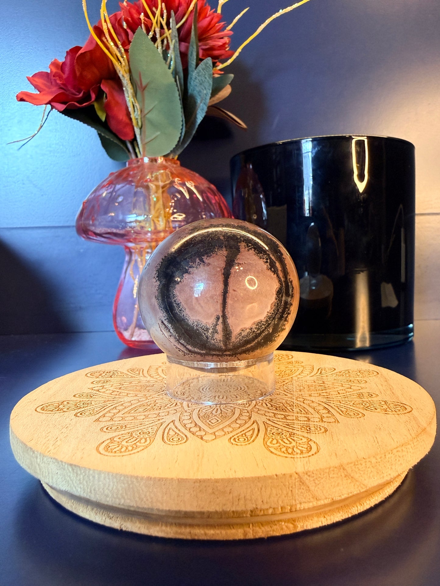 Picture Jasper sphere with intricate design sitting on a decorative coaster in front of a mushroom vase and black jar
