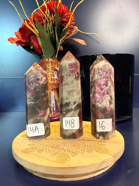 Three purple and grey crystal points on a wooden stand with a flower and labels on a blue surface
