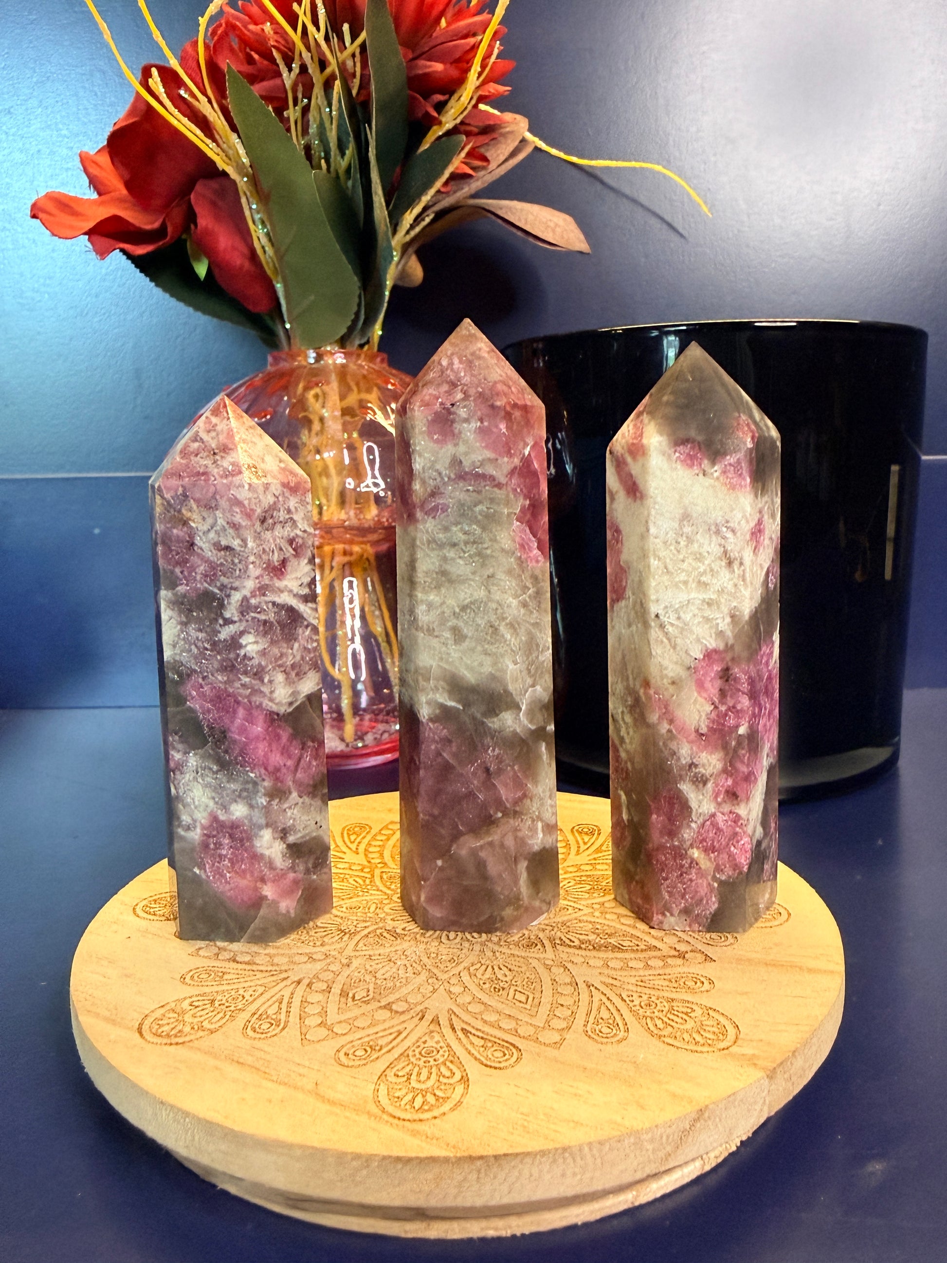 Three purple and grey crystal points on a wooden stand with a flower and labels on a blue surface
