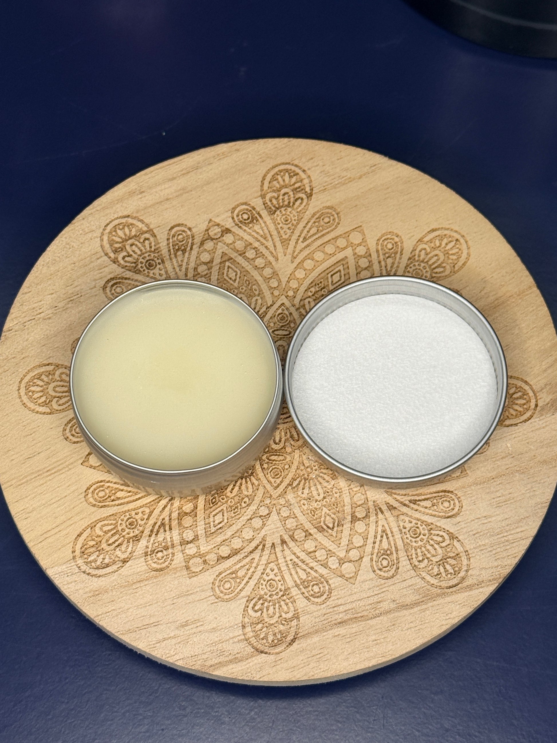 Open circular lip balm container on a decorative wooden coaster on a blue background