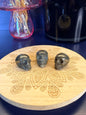 Three dark gold pyrite skulls on a decorative wooden coaster in front of a vase and black jar