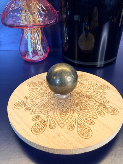 Dark gold pyrite sphere sitting on a decorative wooden coaster in front of a vase and black jar