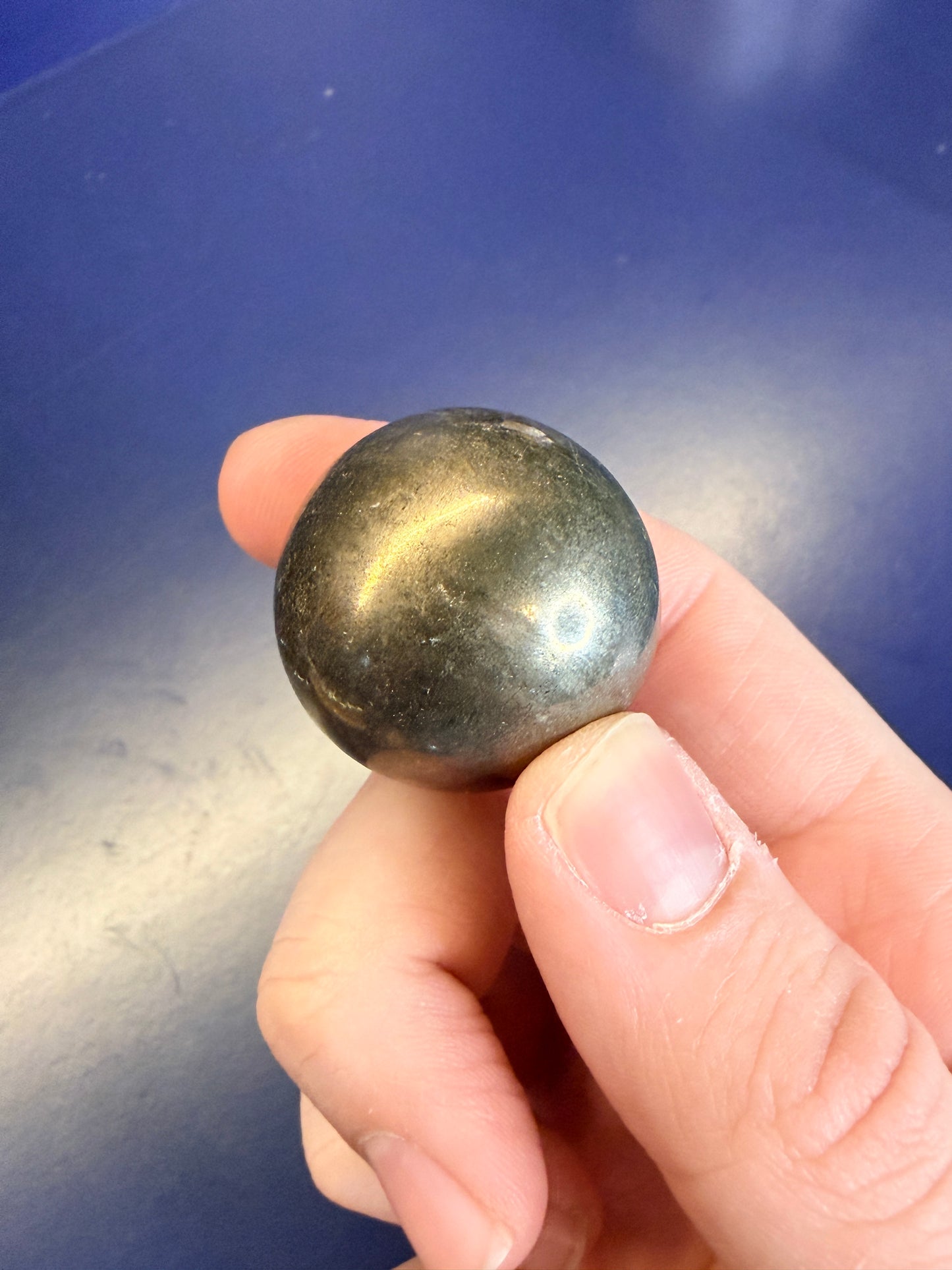 Hand holding a dark gold pyrite sphere in front of a blue background