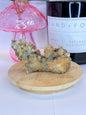 Unique quartz and hematite specimen resting on a wooden coaster in front of a black candle jar and pink vase