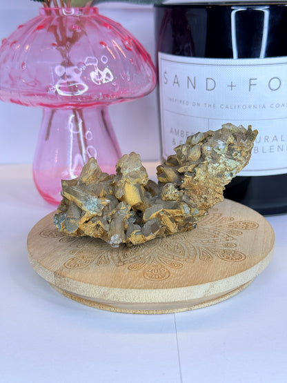 Unique quartz and hematite specimen resting on a wooden coaster in front of a black candle jar and pink vase