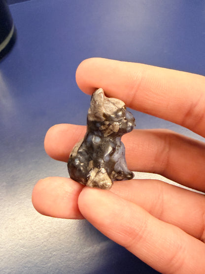 Hand holding a que sera french bulldog crystal against a blue background